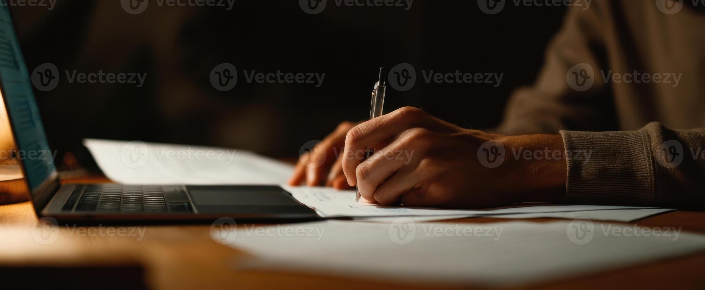 The focused hand writing notes at a modern workspace with a laptop. photo