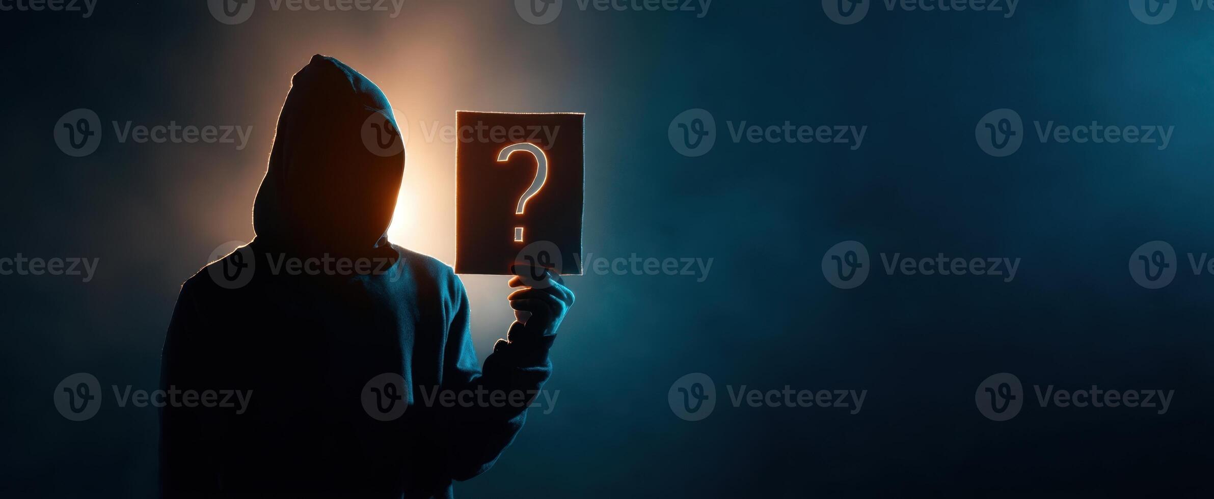 The enigmatic figure holding a question mark sign in a dramatic lighting setup. photo