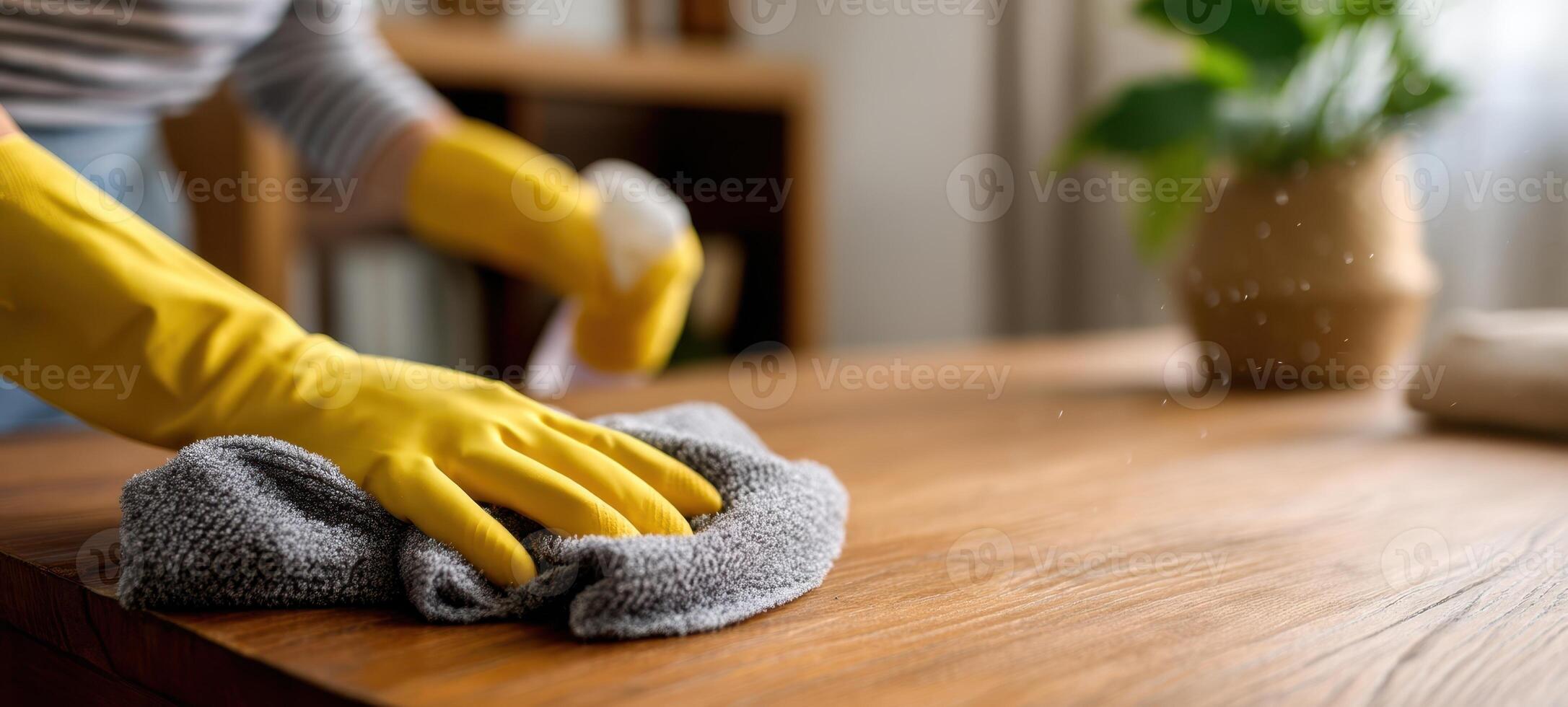 The person cleaning a wooden table with a soft cloth and spray. photo