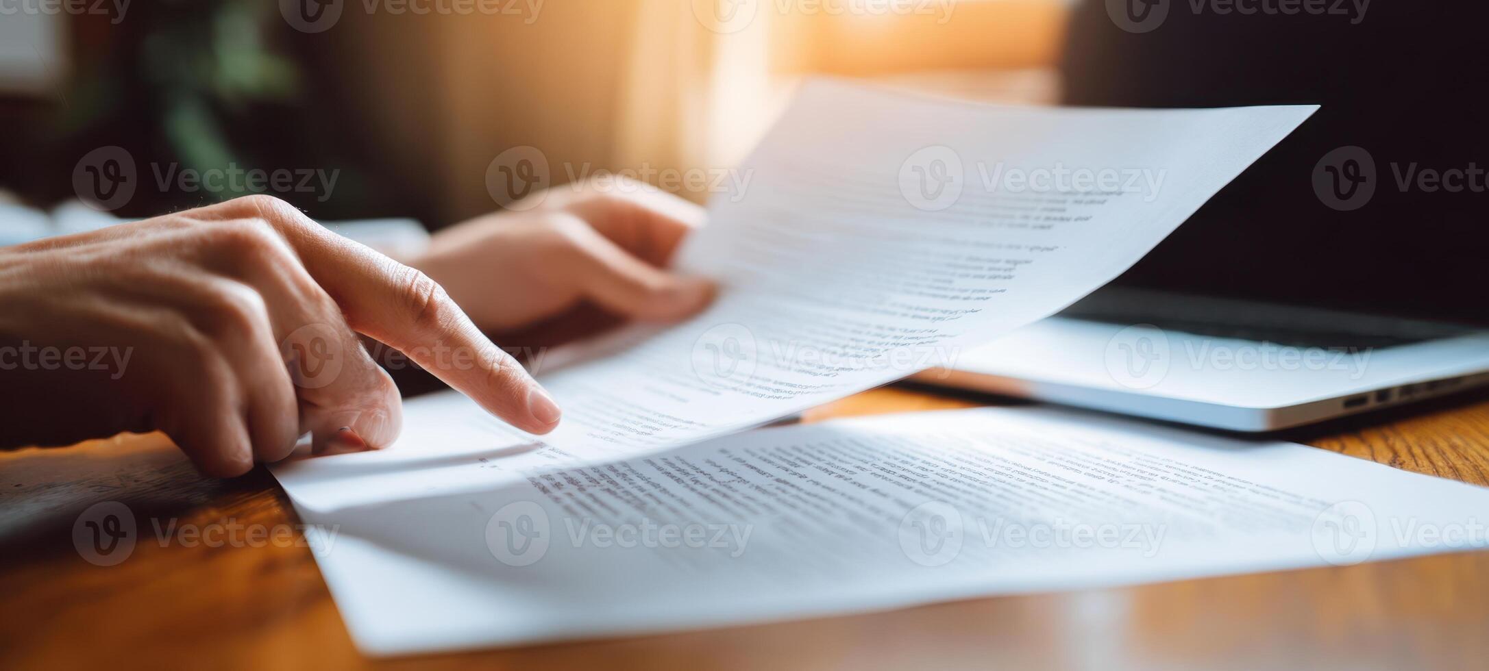 The hands reviewing important documents beside a laptop in a bright workspace. photo