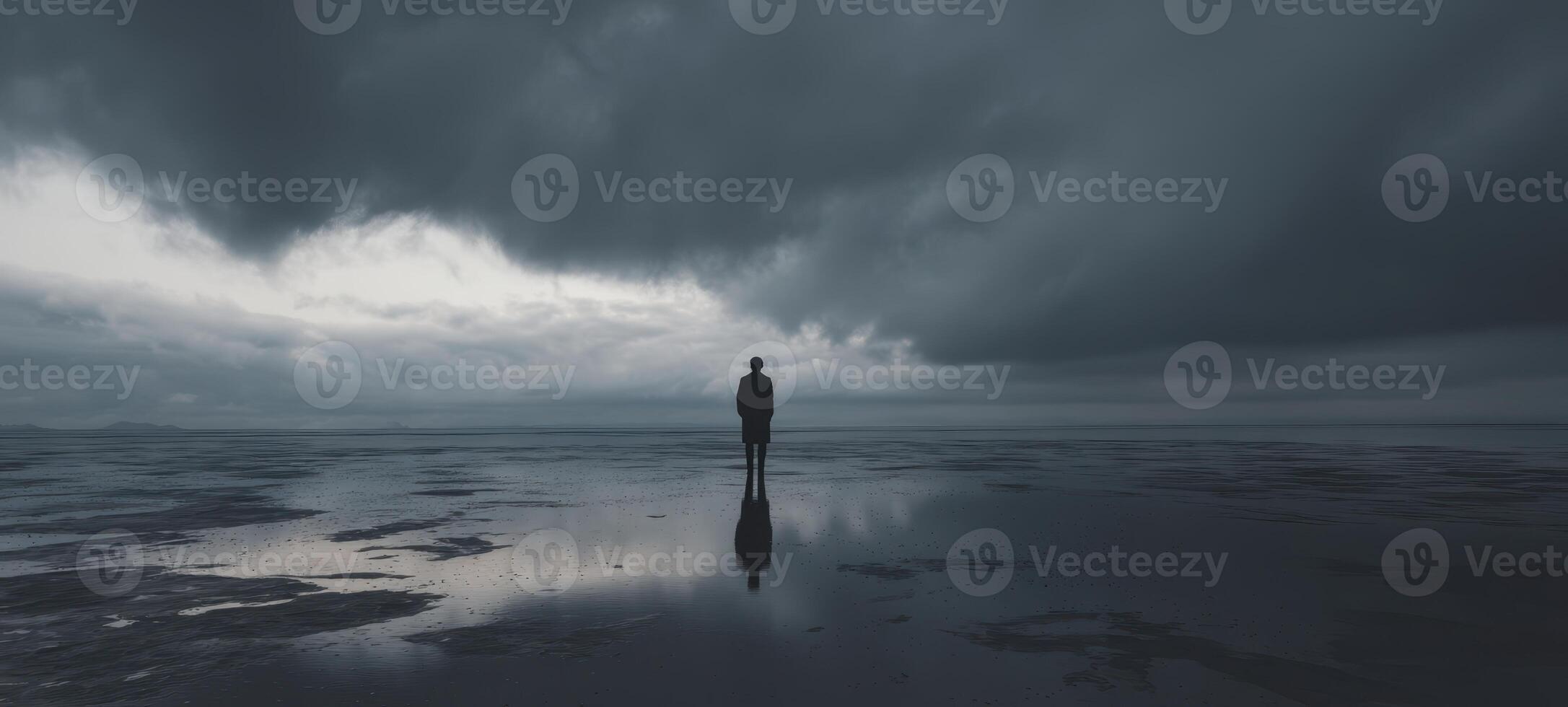 The solitary figure standing still on a reflective shoreline under dark skies photo