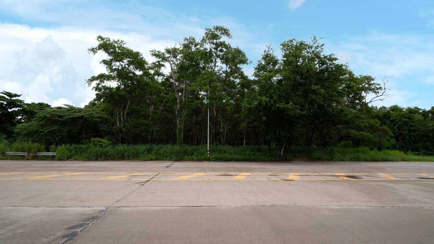 Horizontal and Landscape view of concrete road with yellow line. Background of green forest with lighting pole and gardens. Under blue sky and white clouds. photo
