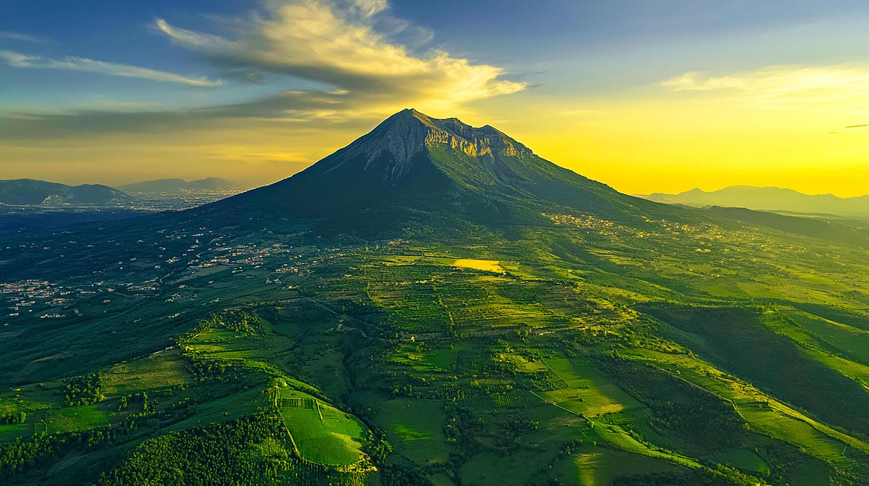 Green grass and clouds cover the mountain landscape under the morning sky, while a sunset paints the distant mountains photo