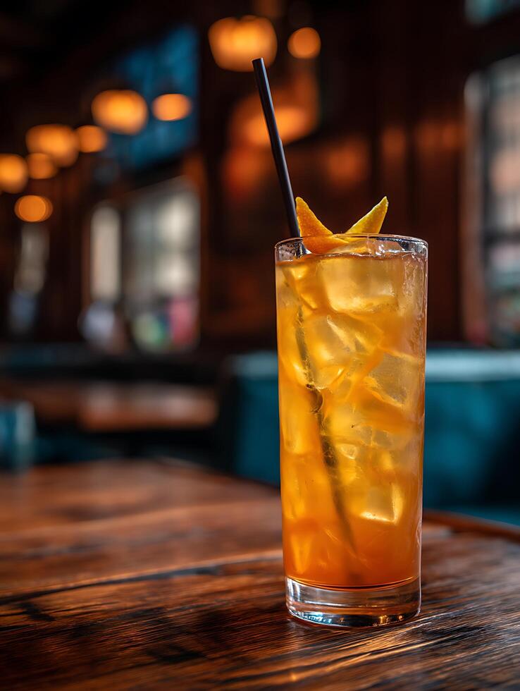 Refreshing Iced Tea Cocktail in a Rustic Bar Setting. A close up image of a tall glass filled with amber iced tea, ice cubes, and an orange peel garnish. photo