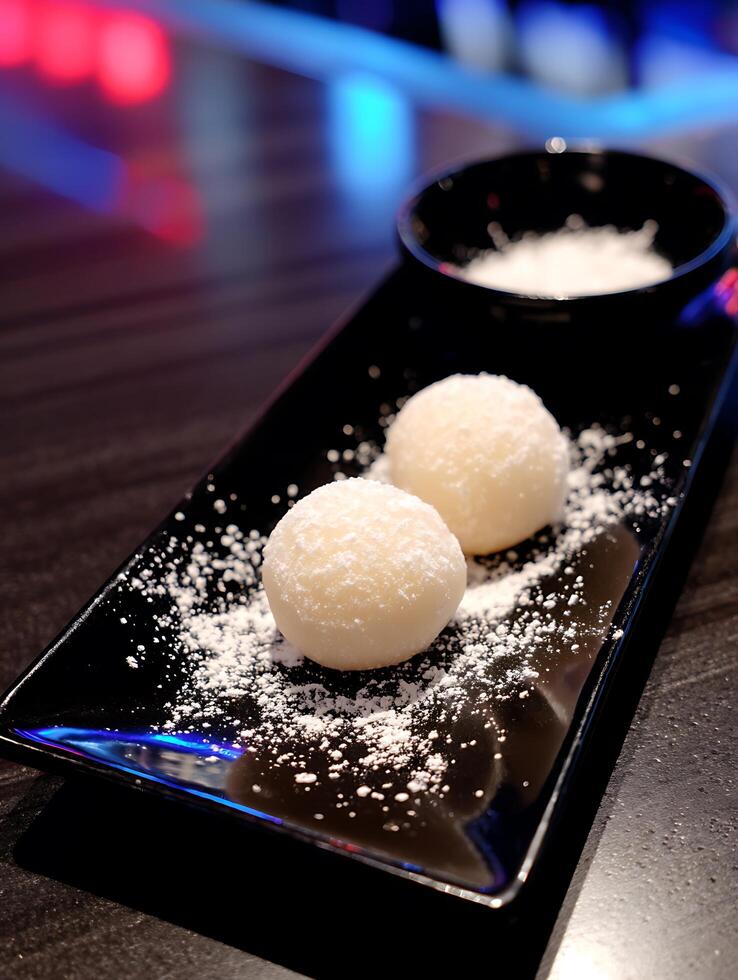 Close up of Two Mochi Balls on a Black Plate with Powdered Sugar. photo