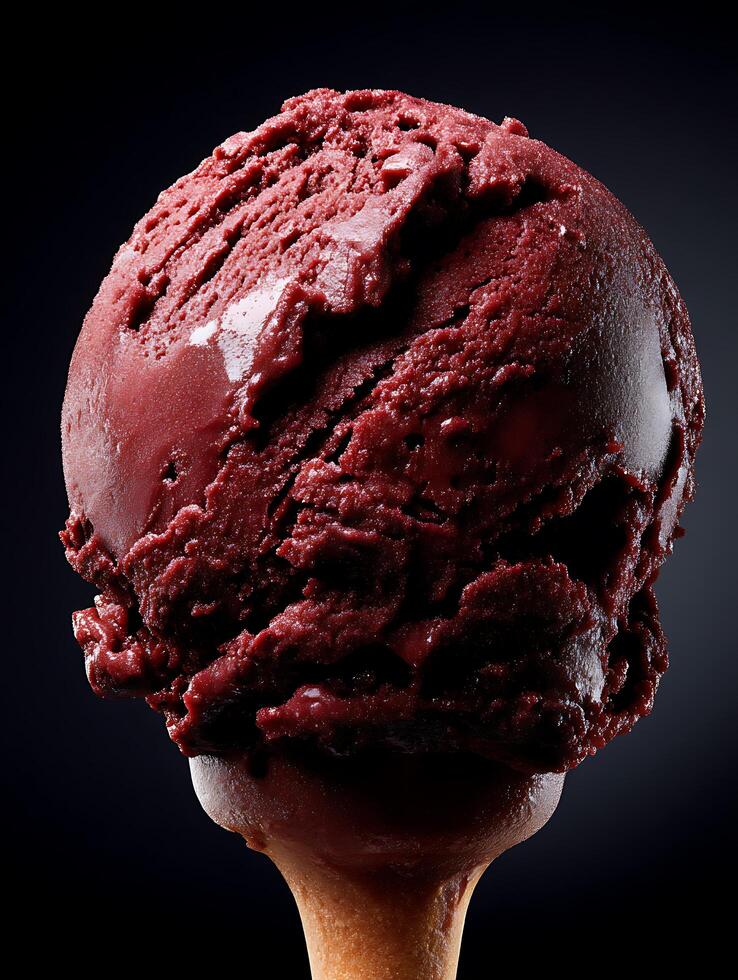 Close up of a delicious scoop of dark red ice cream on a cone against a black background. photo