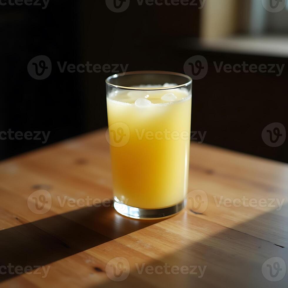 Refreshing Yellow Drink with Ice Cubes on Wooden Table in Sunlight photo