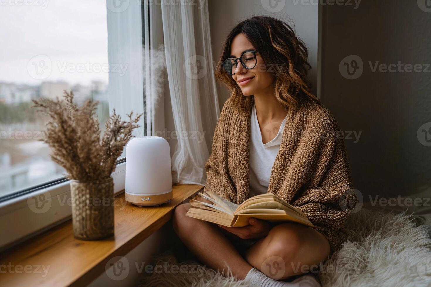 woman enjoying aromatherapy with diffuser in cozy reading nook, self love moment photo