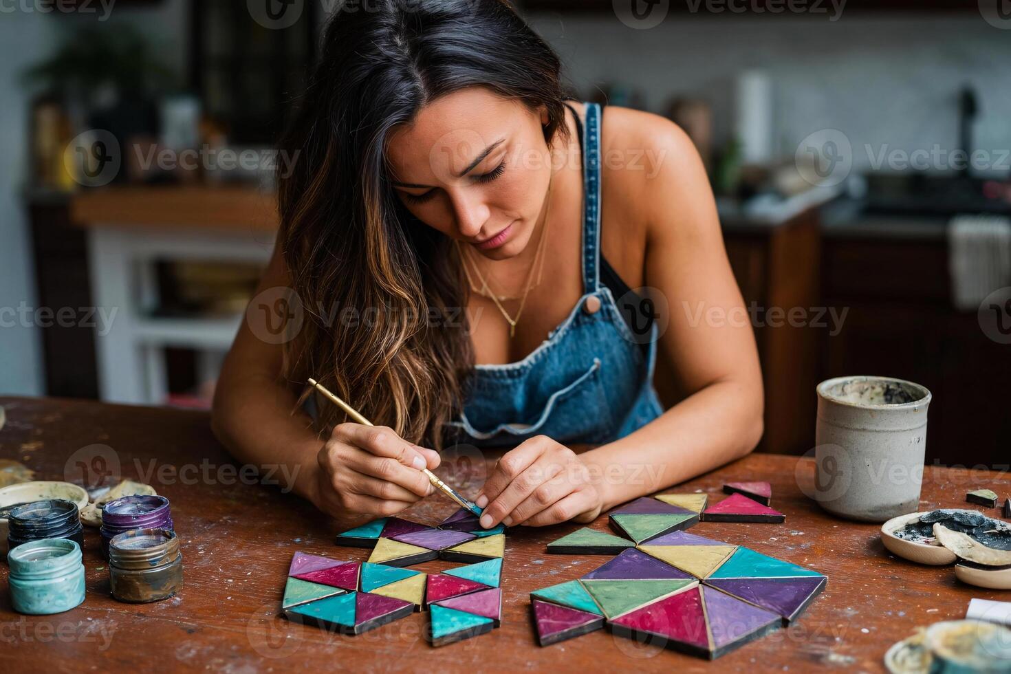 Woman paints abstract patterns on hand cut wood shapes, creating modern handmade wall art photo