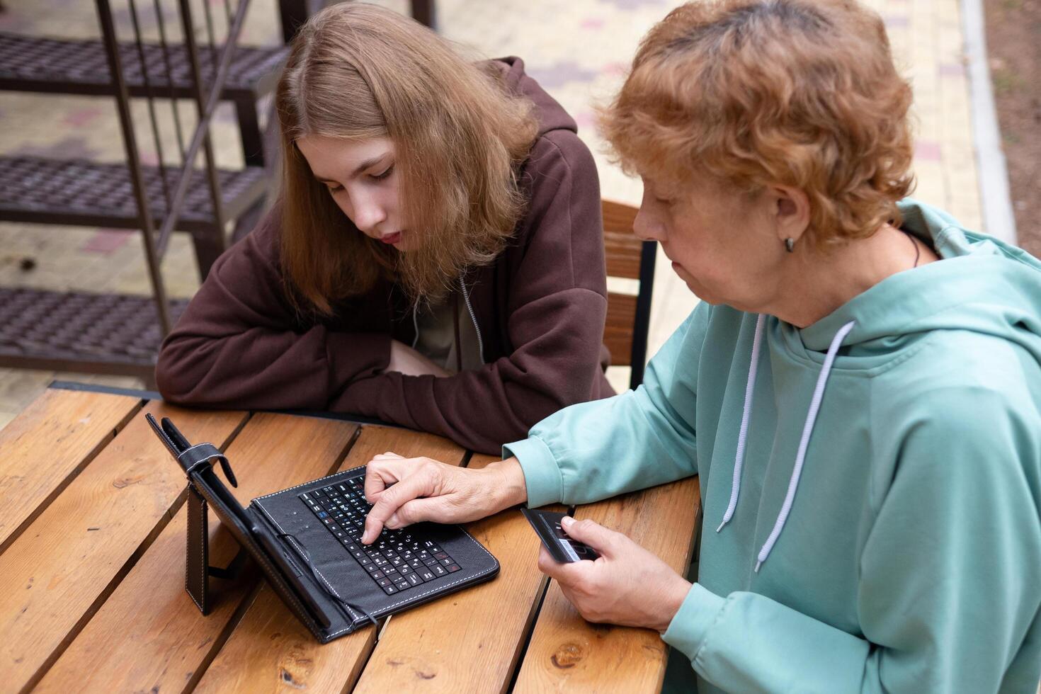 The image features two women, an elderly woman and a young woman, sitting at a table with a laptop photo