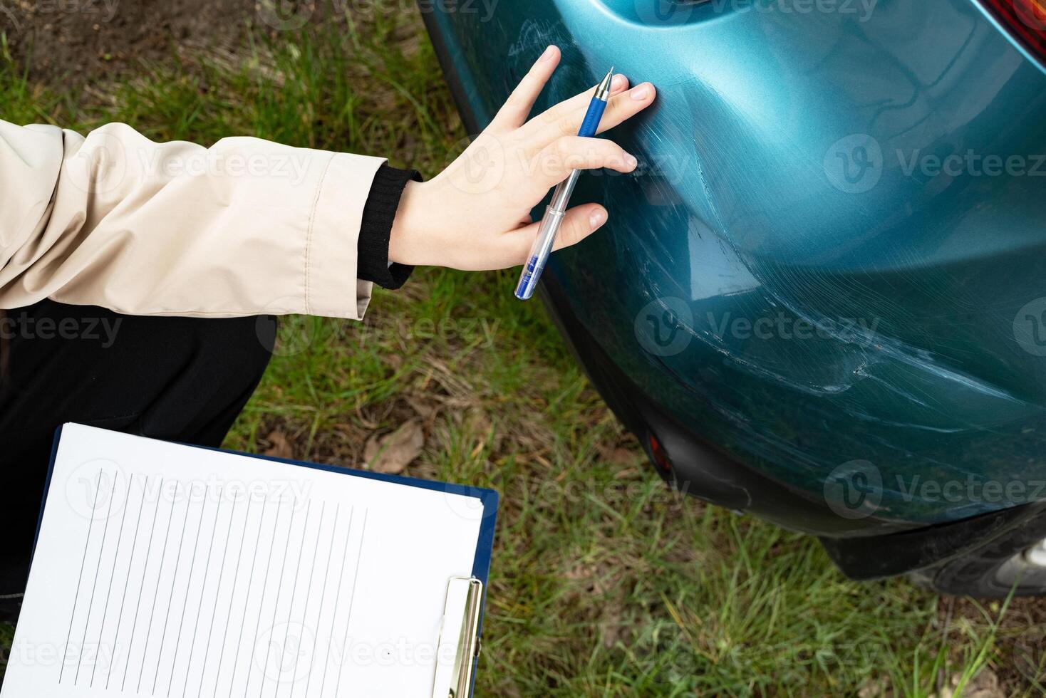A close-up of a damaged car bumper with a person filling out a form on a tablet, getting insurance. photo