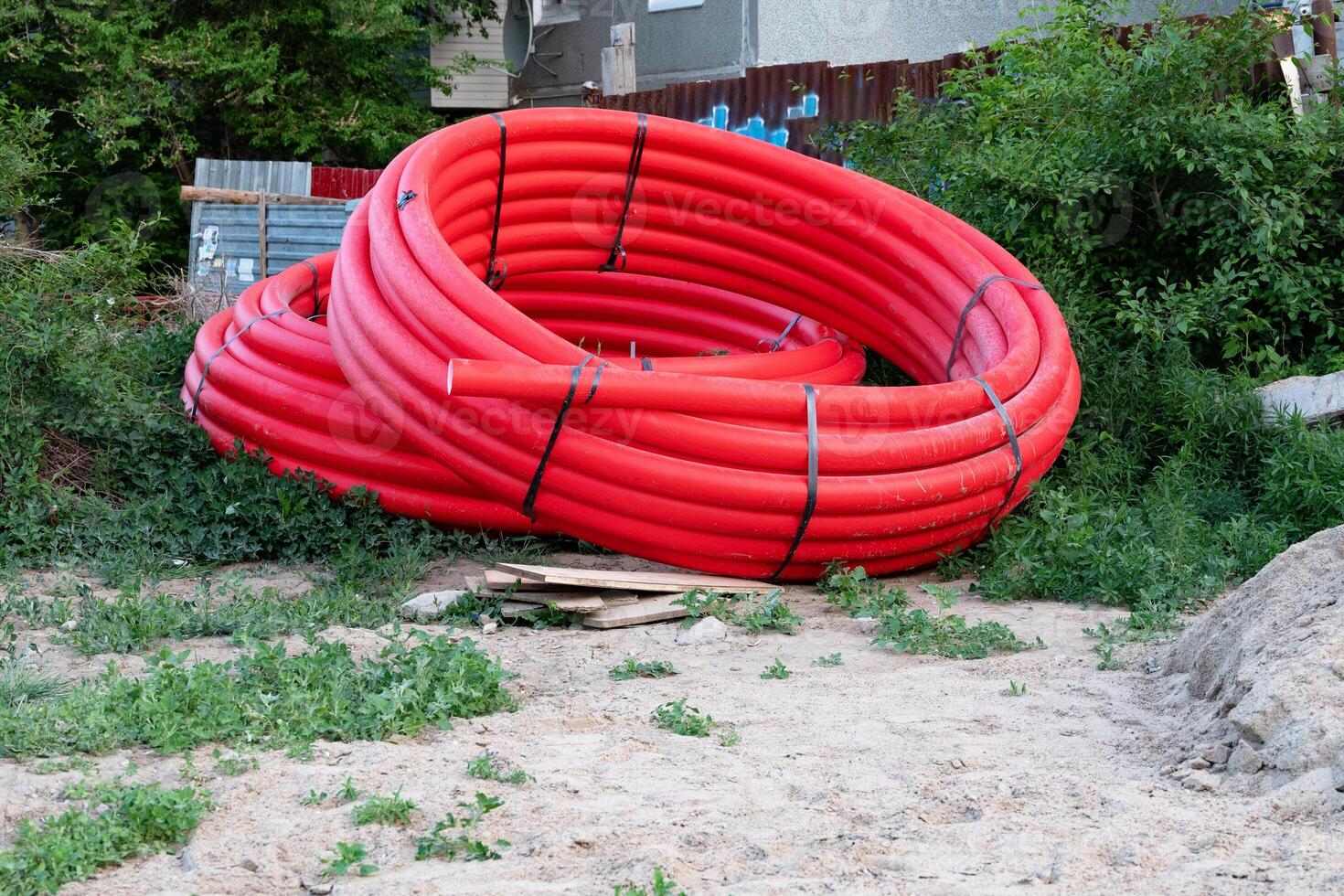 Close up view looking down on large shiny black drain drainage sewer pipes stacked at a construction site with orange red net safety fencing photo