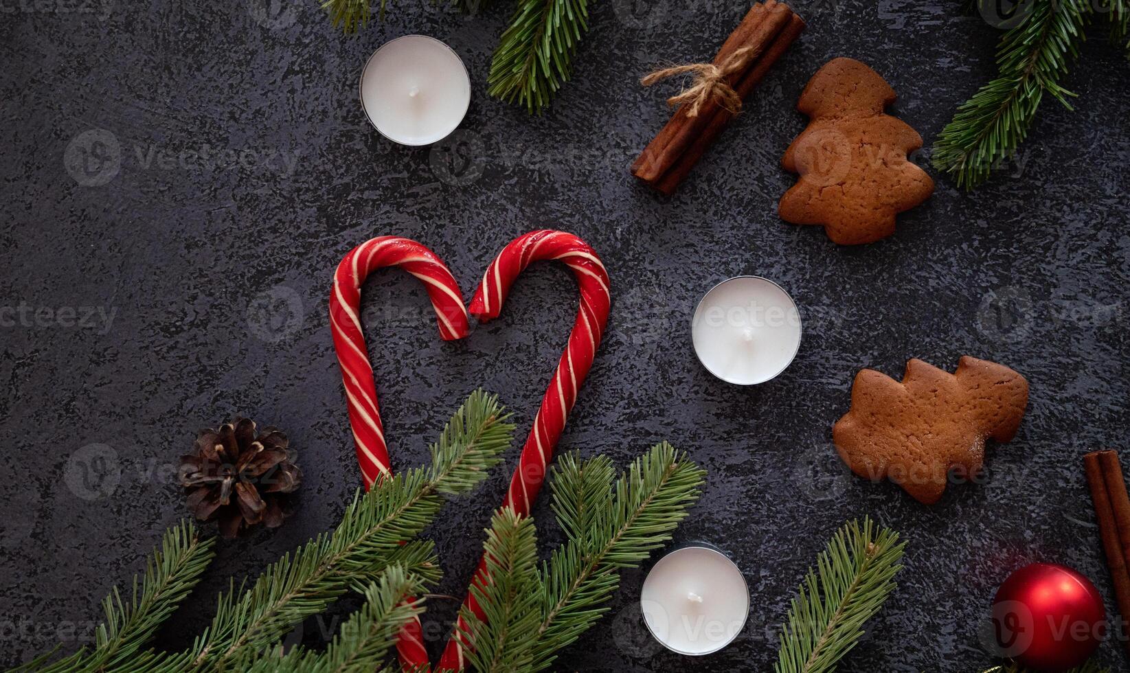 A festive flat lay featuring Christmas decorations, including candy canes forming a heart shape, gingerbread tree cookies, cinnamon sticks, pine branches, candles, and a red ornament photo