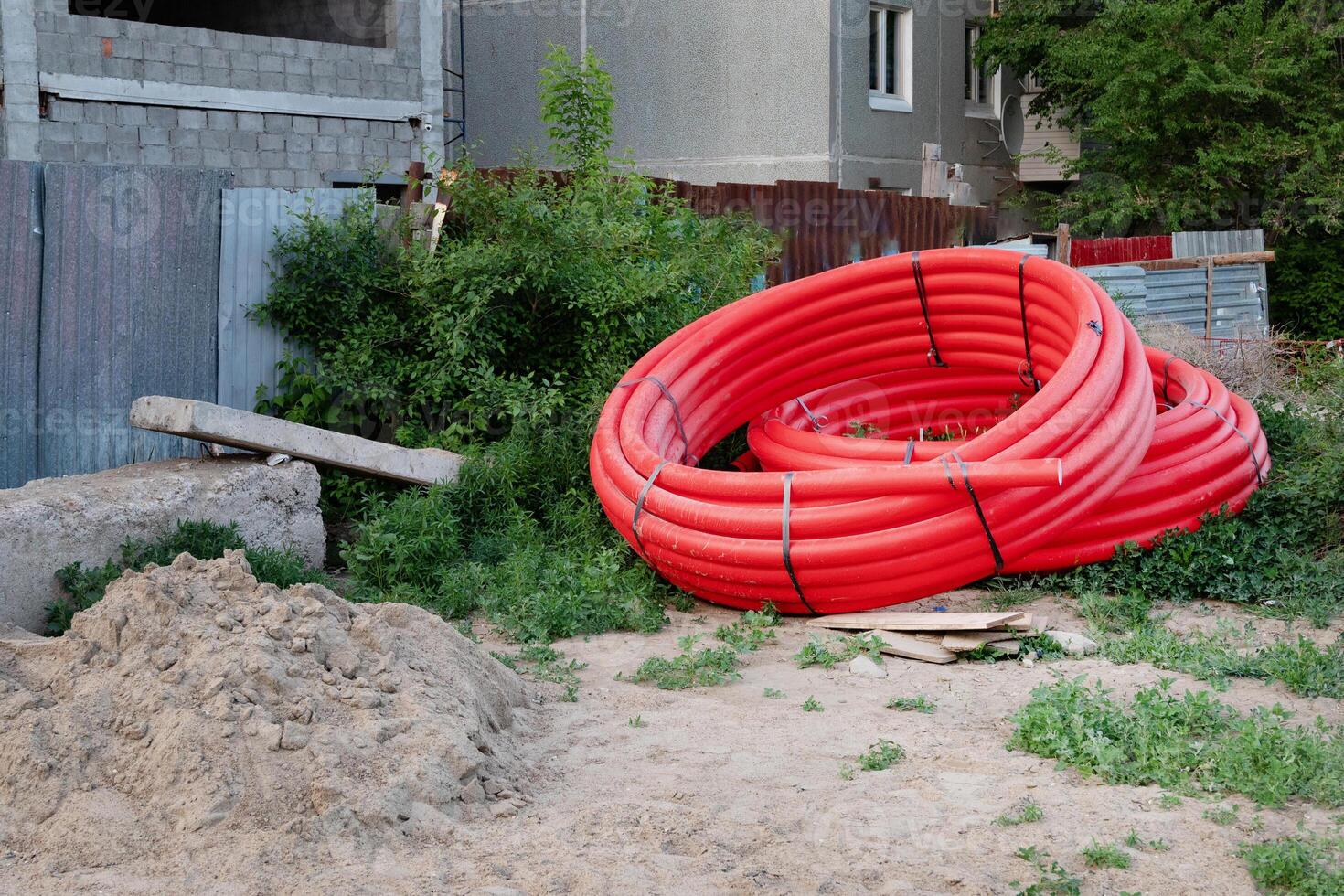 view looking down on large shiny black drain drainage sewer pipes stacked at a construction site with orange red net safety fencing photo