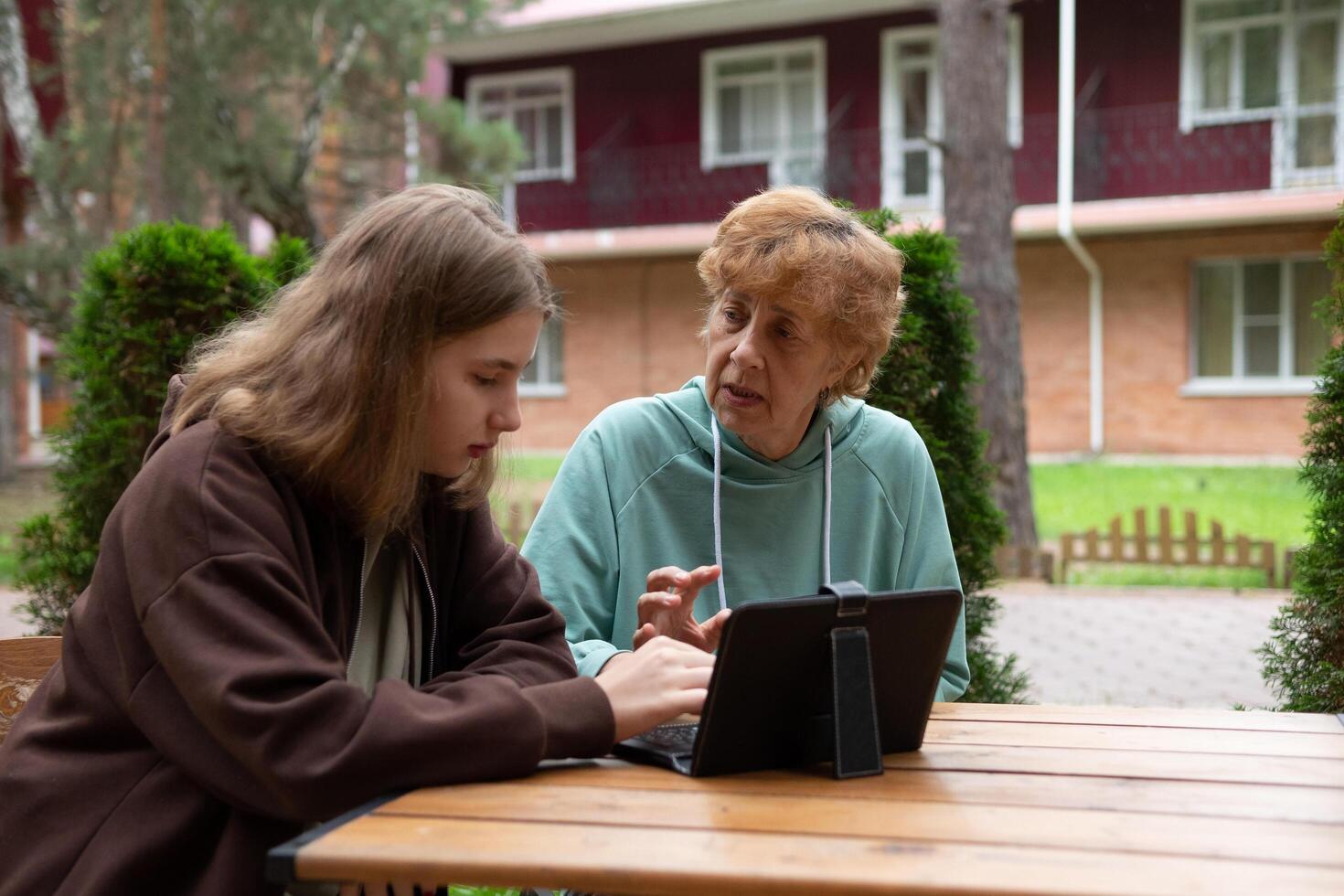A grandmother and granddaughter are sitting outside, possibly shopping online, as the grandmother holds a credit card and smiles while looking at a laptop. photo
