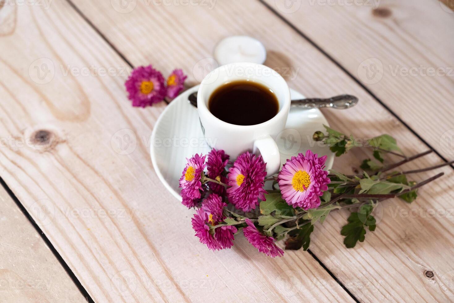 Overhead shot of an autumn-themed arrangement with a coffee cup as the central focus, surrounded by red macarons, flowers, leaves, acorns, and a candle. photo