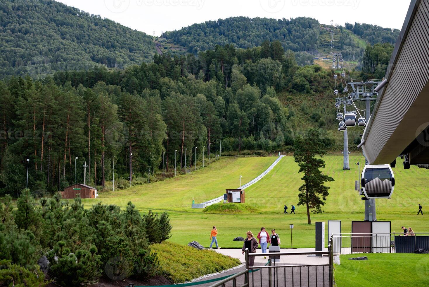 The image shows a scenic mountain landscape with a green grassy slope and a cable car system running up the hill. photo