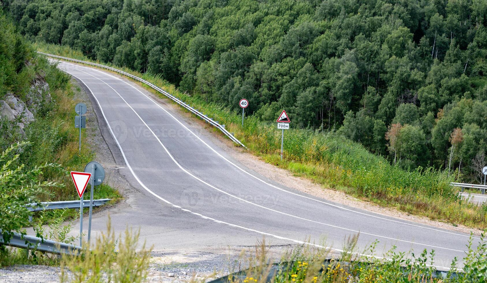 Curved road with traffic signs surrounded by lush greenery. photo