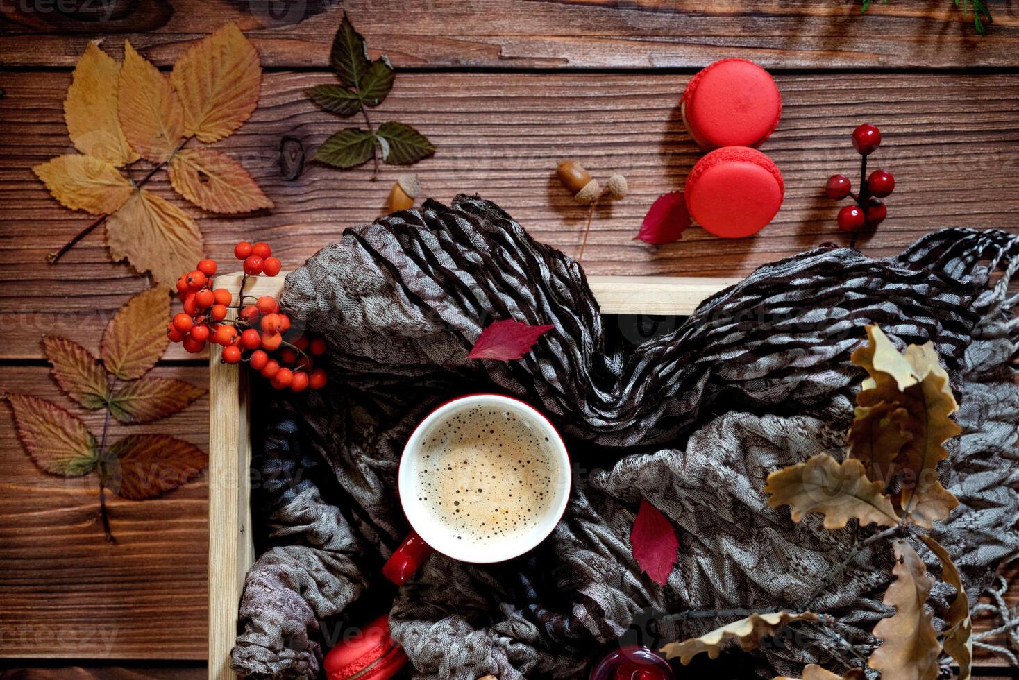 An aesthetic autumn flat lay composition, highlighting a cup of coffee, red macarons, purple flowers, leaves, acorns, and a candle on a textured background. photo