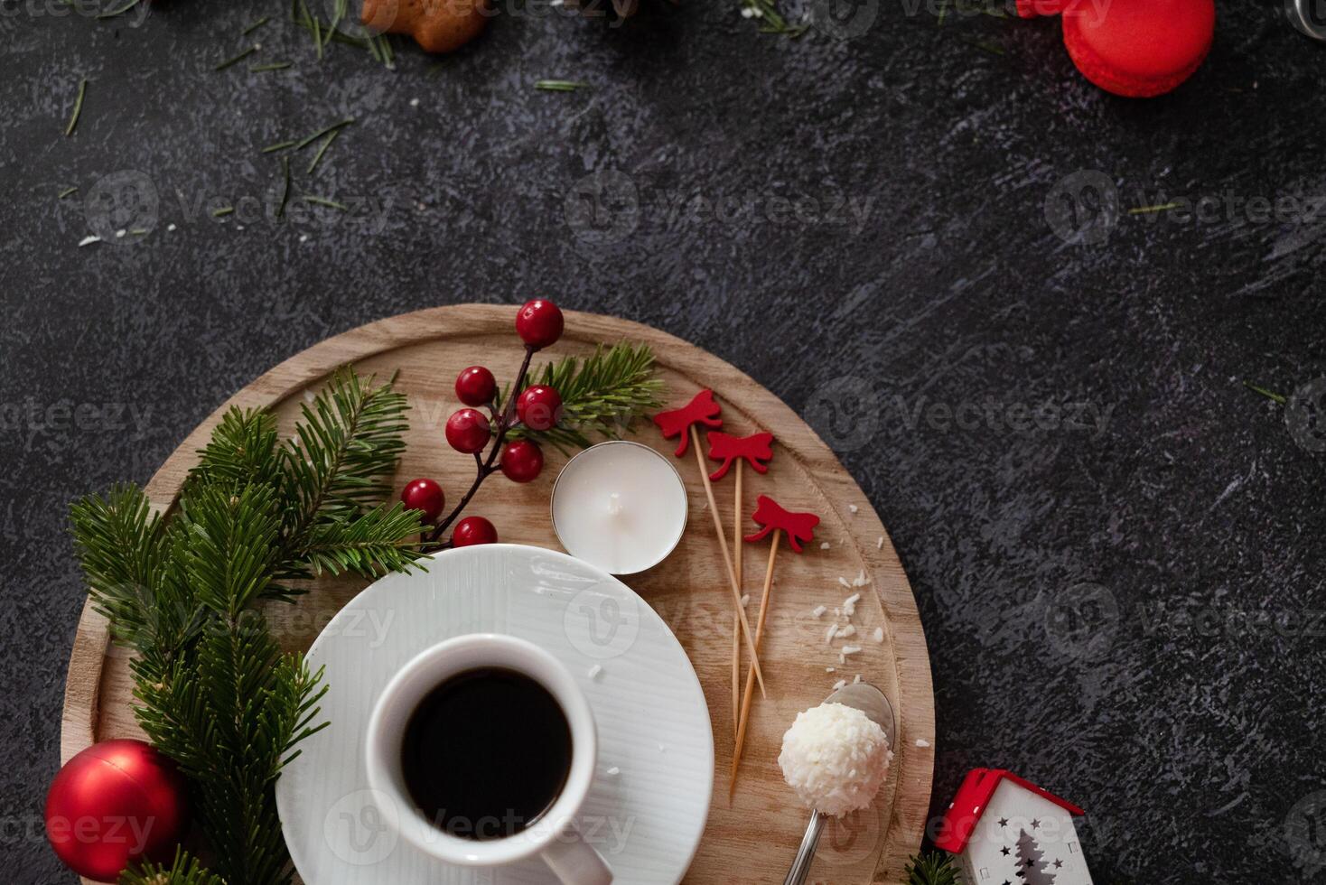 A comforting image of a coffee cup surrounded by Christmas treats and decorations, including gingerbread cookies, cinnamon sticks, candy canes, and candles, on a dark, festive background. photo