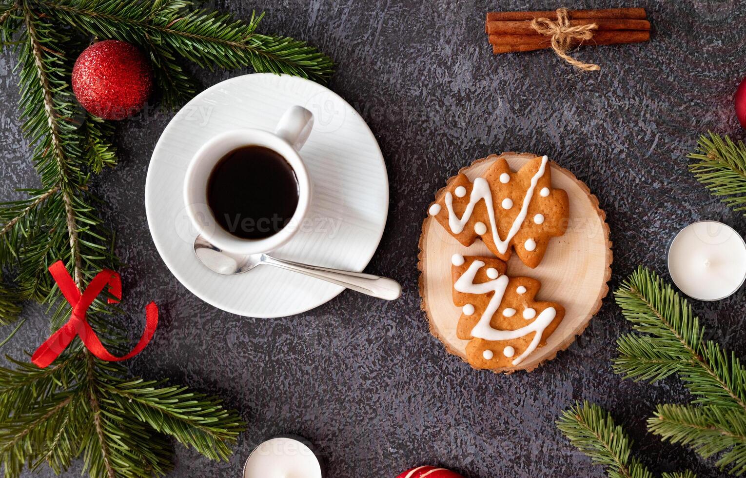Close-up of a Christmas table arrangement with a coffee cup, gingerbread cookies, cinnamon, candy canes, candles, and pine branches creating a festive ambiance. photo