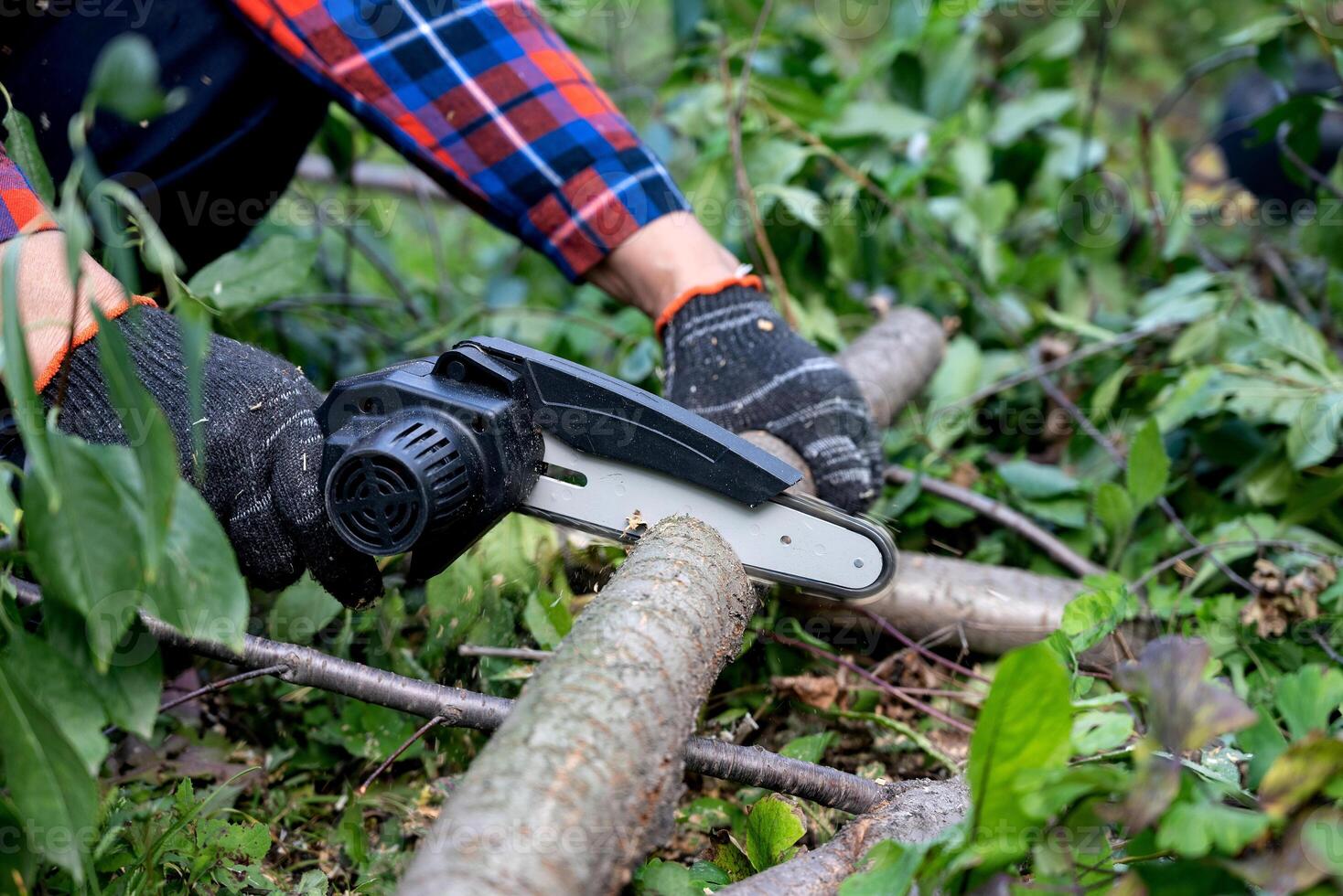 A man in gloves saws a wooden tree trunk with a saw. photo