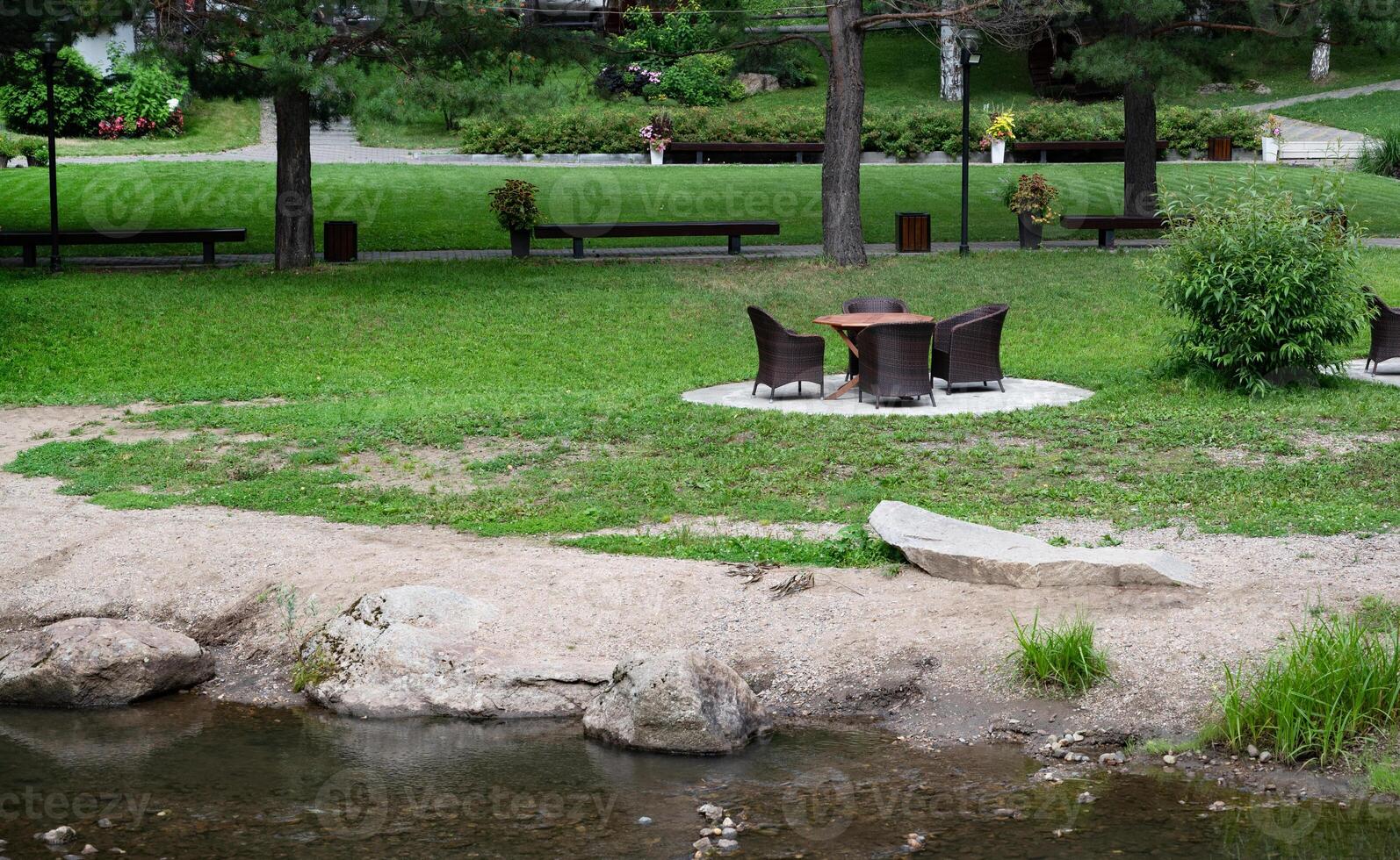 Outdoor wicker furniture set by a stream in a lush garden. photo