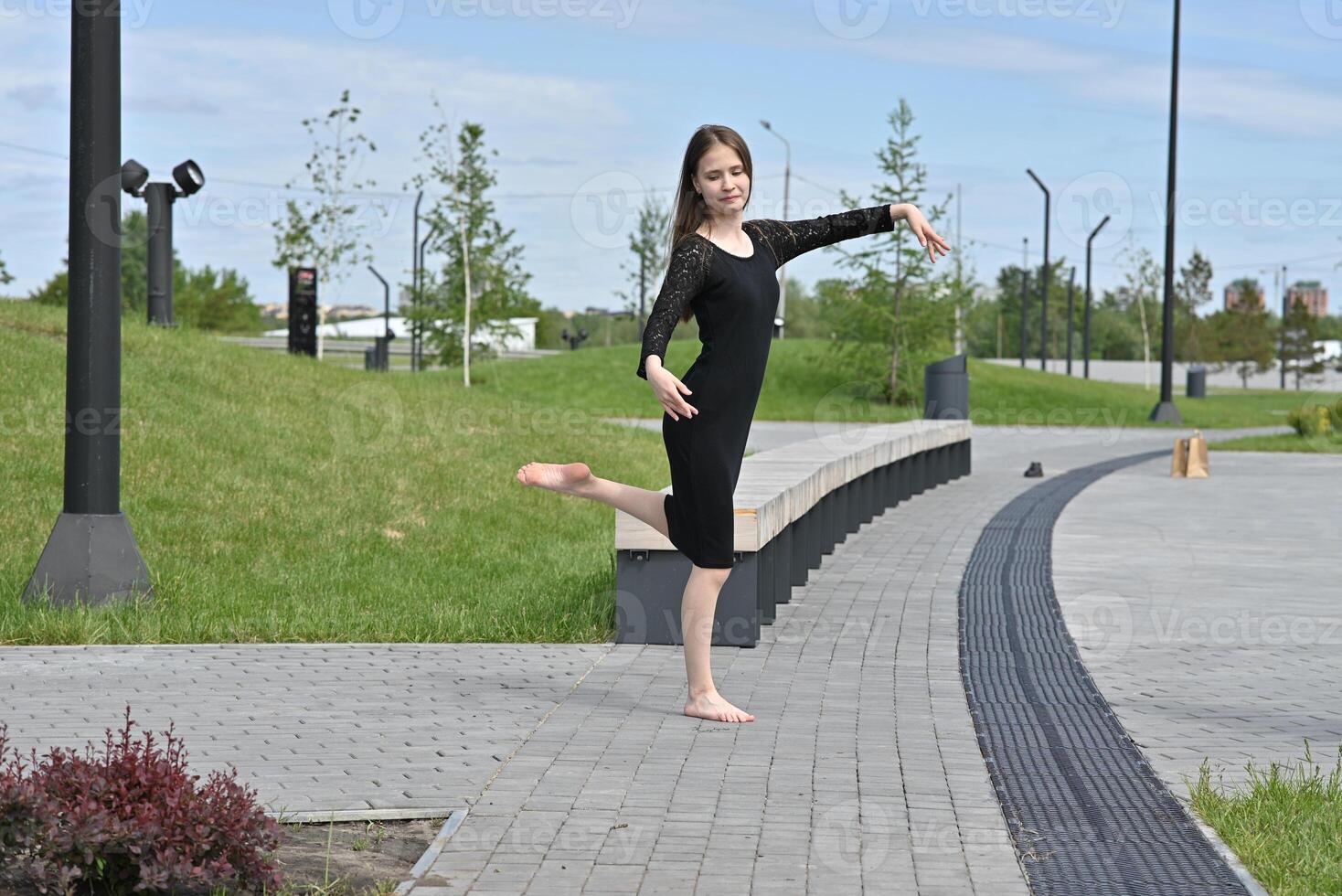 A woman calmly waiting in front of a parking lot entrance, with city buildings and cars in the background. photo