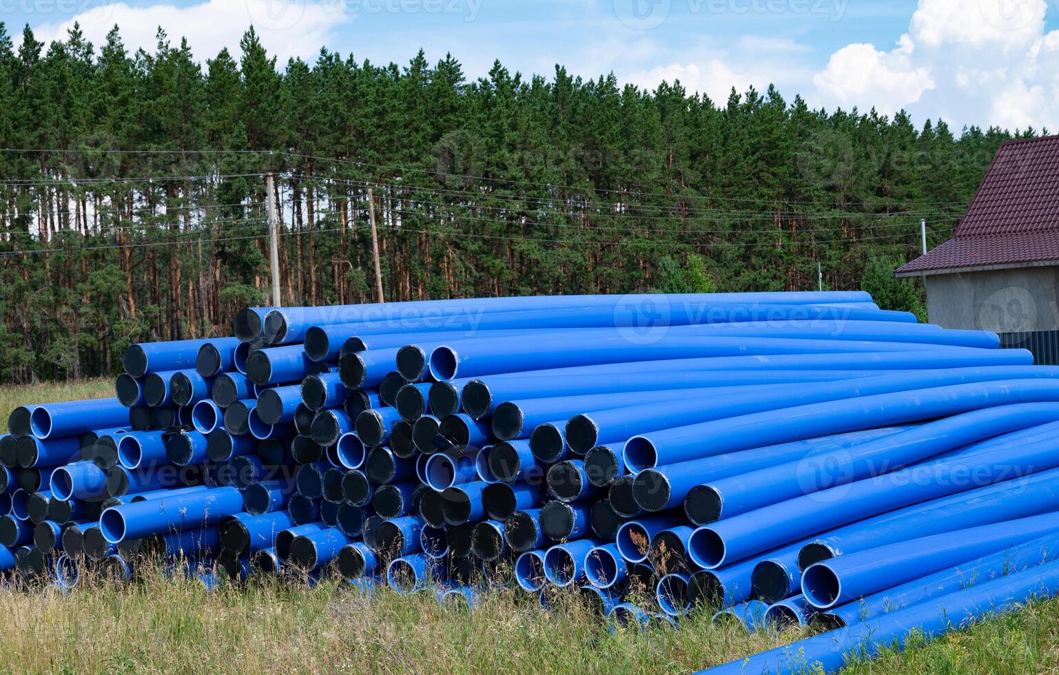 Stacked blue pipes resting in a field near a forest during daylight photo