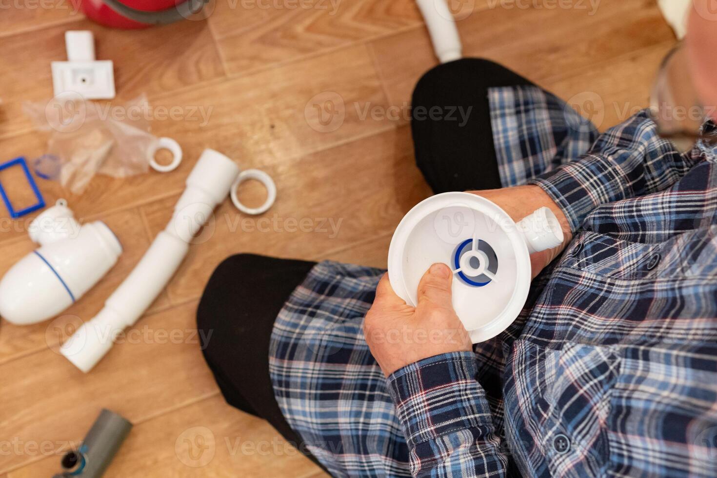 Person assembles plumbing fixtures while sitting on a wooden floor in a home renovation project photo