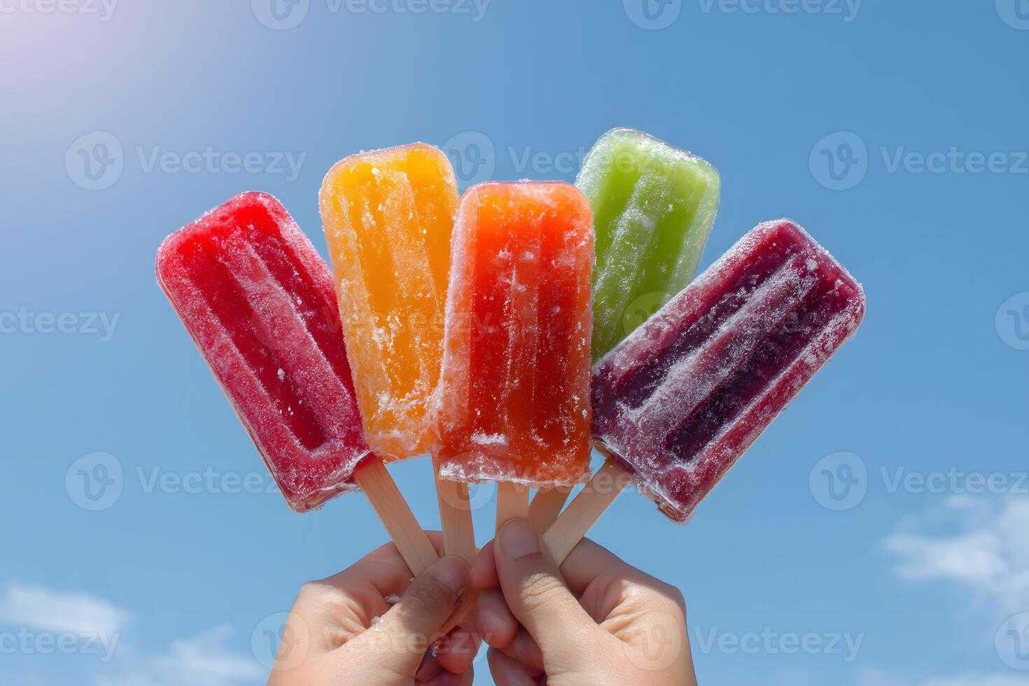 Hands holding assorted colorful ice pops against clear blue sky on a warm summer day photo