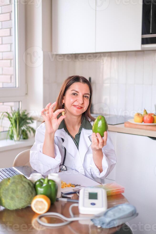 Nutritionist with avocado and capsule of dietary supplement at table with healthy products. Avocado is rich in omega-3 and helps in weight control. Dietetics concept, health. photo