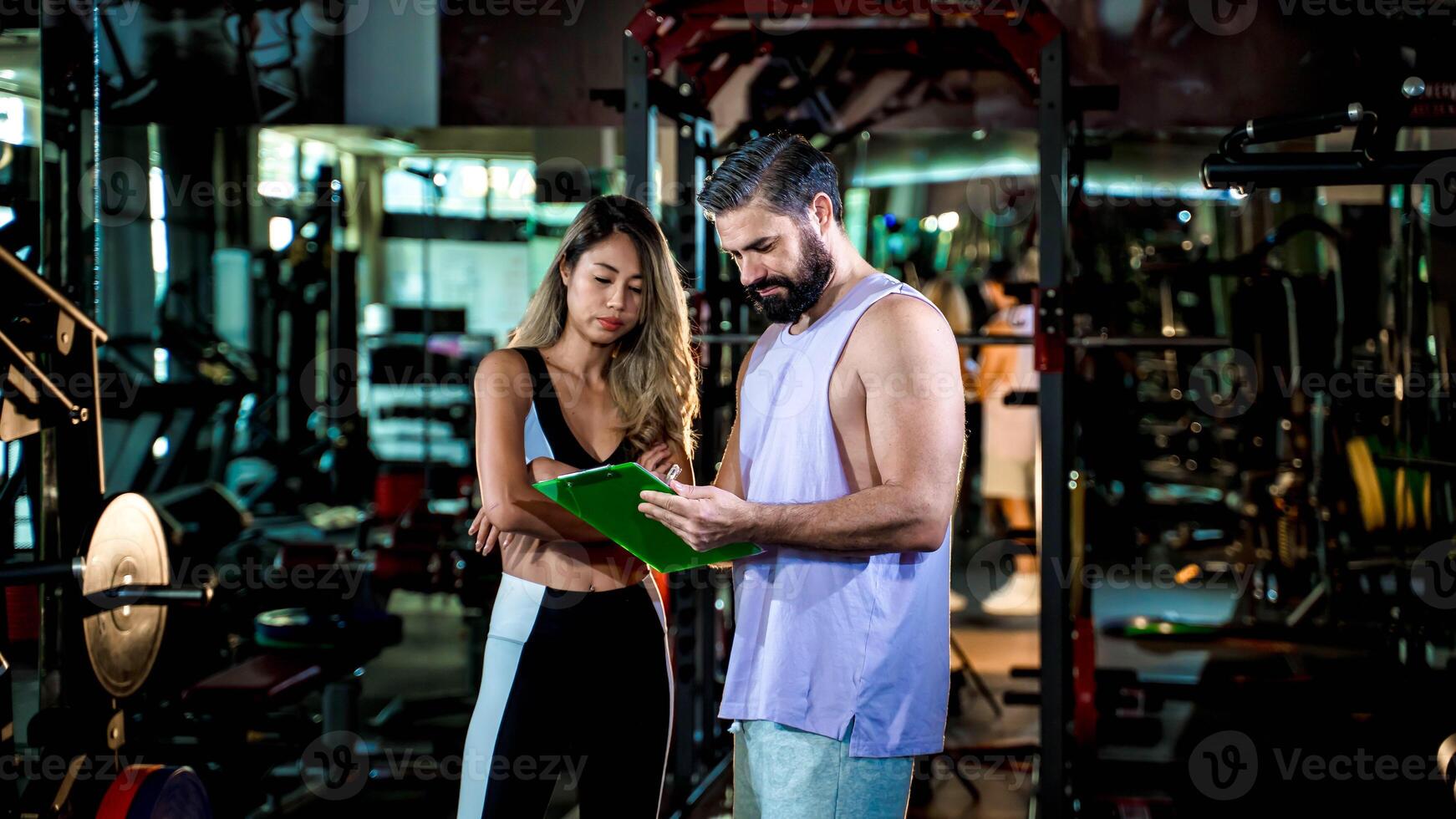 Fitness trainer reviewing personalized workout plan with female client inside modern gym, coaching, planning, and fitness goal setting session for success photo