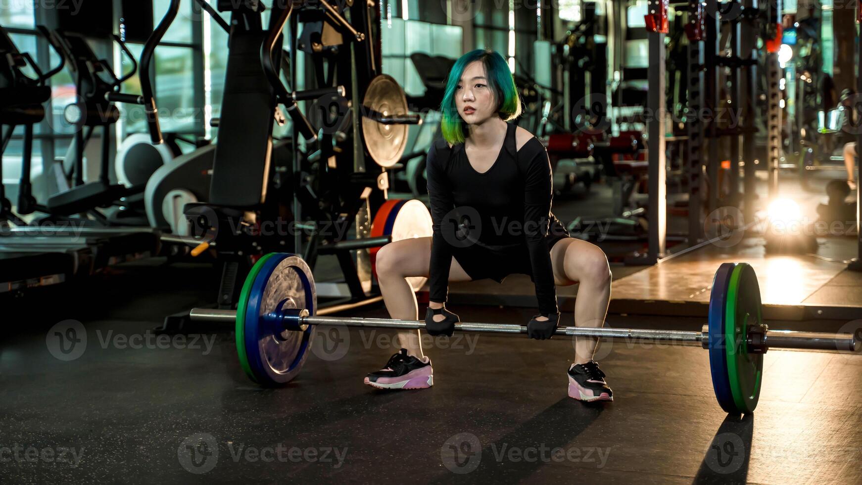 Strong young woman preparing for sumo deadlift with heavy barbell in gym, wearing black athletic outfit, focus and power in strength training photo