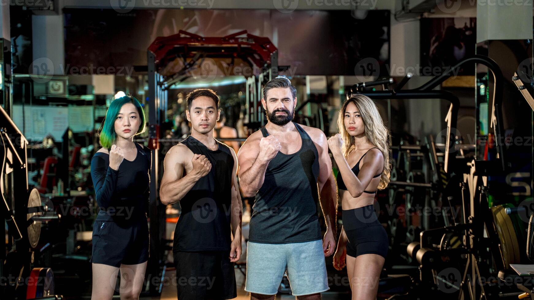 Confident diverse fitness team standing strong together in gym, raising fists as a symbol of unity, empowerment, and motivation for healthy lifestyle and teamwork. photo