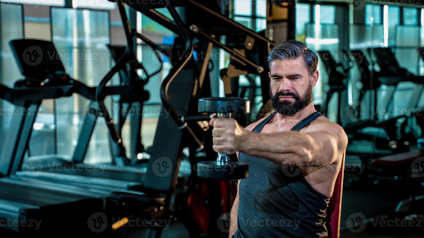 Strong mature man concentrating on seated dumbbell exercise in gym, building muscle with intense focus and dedication for healthy lifestyle photo