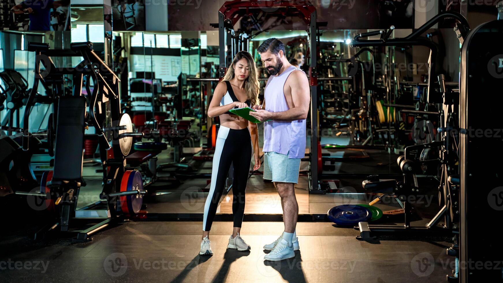 Personal trainer discussing workout plan with female client at modern gym, fitness consultation, coaching, and customized training program for healthy lifestyle success photo