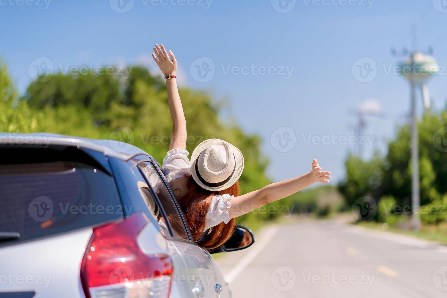 Happy young woman enjoying a summer road trip with arms out of car window, feeling free and joyful while traveling on a bright sunny day through the countryside. photo