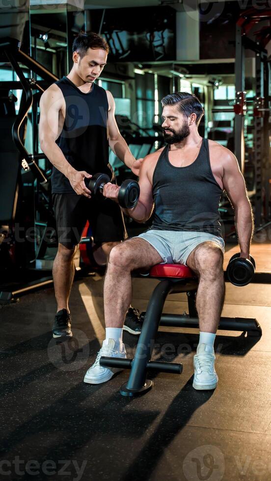 Personal trainer assisting man with seated dumbbell bicep curls at gym, emphasizing proper technique, strength training, and fitness motivation for muscle growth. photo