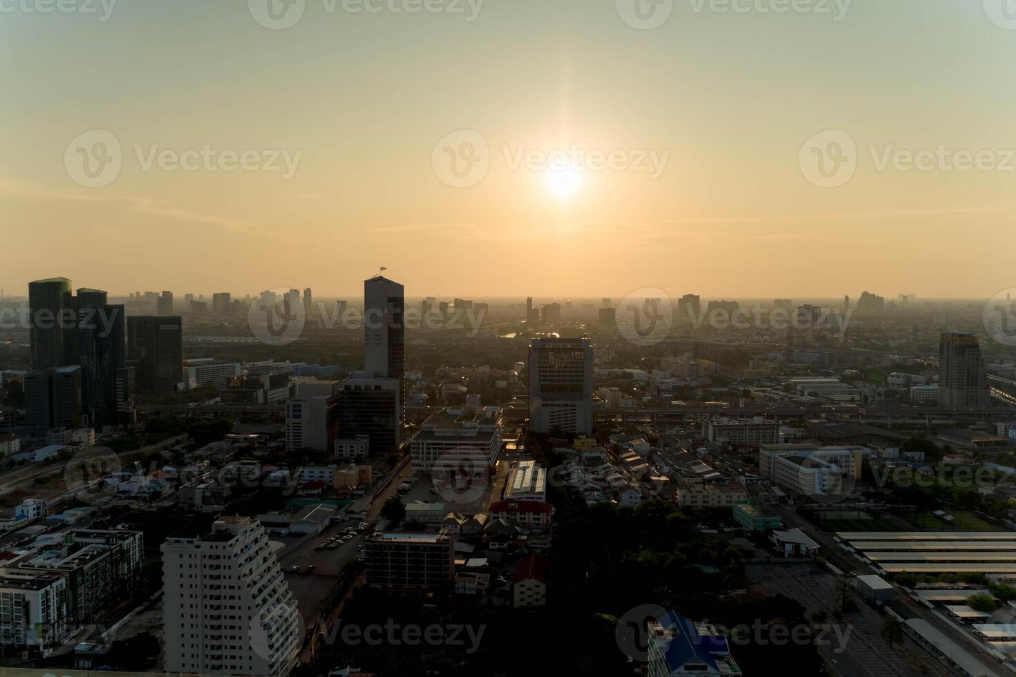 Scenic aerial view of a modern city skyline at sunset with golden sunlight illuminating tall buildings, roads, and urban landscape under a hazy evening sky photo