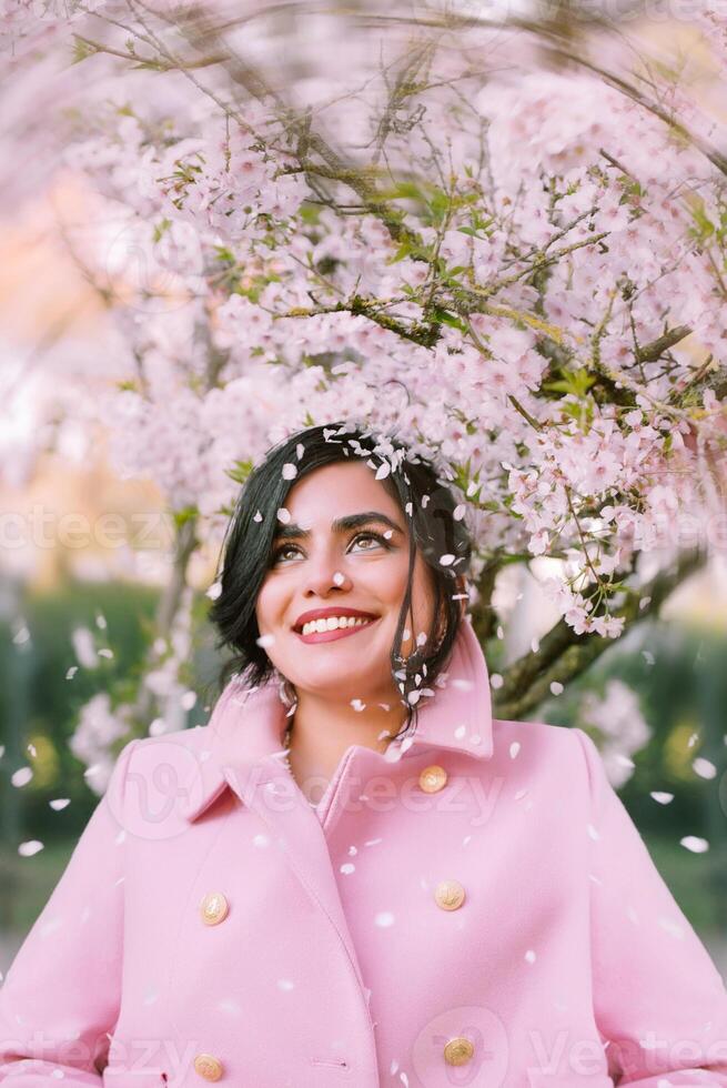 Portrait of a beautiful woman in pink coat under cherry blossom in spring photo