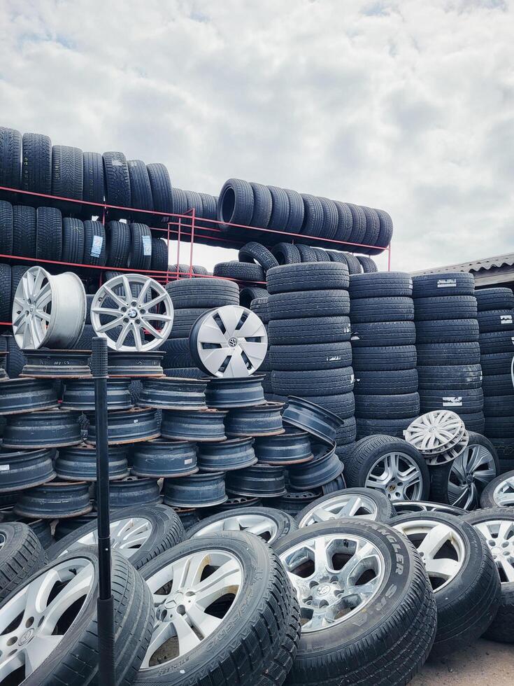 Vilnius, Lithuania, 2025 - Wall of used rubber, old alloy wheels, and piled tires at a tire service area of an auto parts market photo