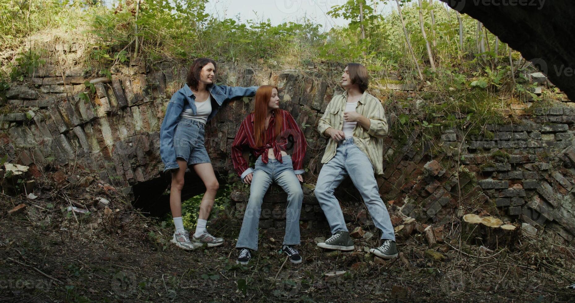 Three friends are smiling and talking standing near a ruined historical building. The man smokes. A sunny summer day photo