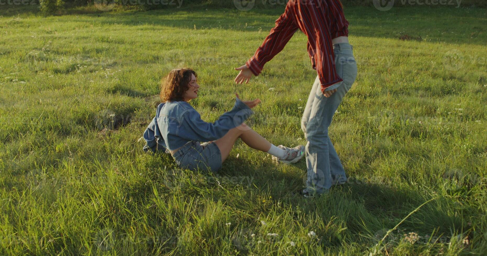 A young woman helps her friend get up from the grass. Relaxing in the field on a sunny summer day photo