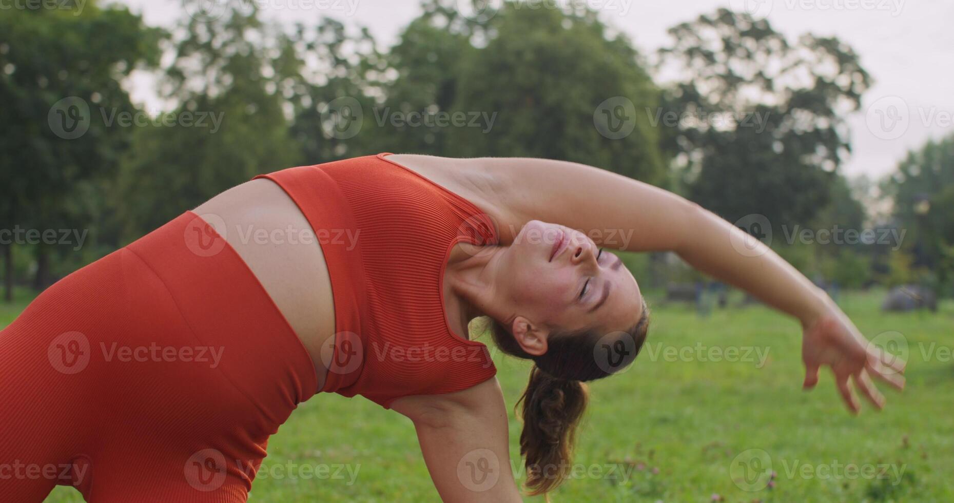 A woman in late pregnancy in sports clothes is doing Pilates in a city park. She smiles at the camera photo