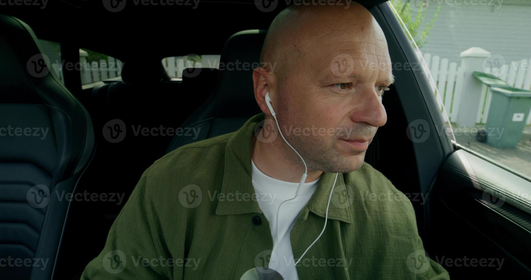 A man with earphones gathers his things and gets out of the car. Front view from the car interior. Summer day photo