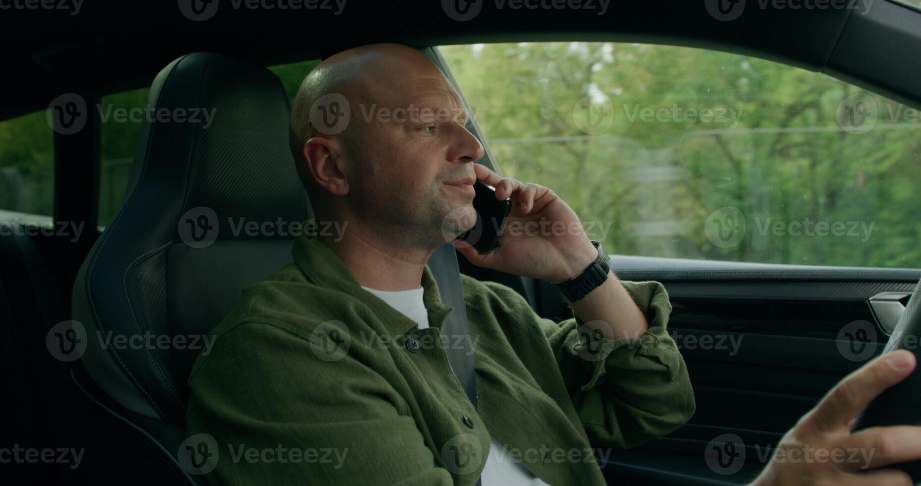 A man is talking on a mobile phone while driving a car. He's smiling. View from the car interior. Summer day photo
