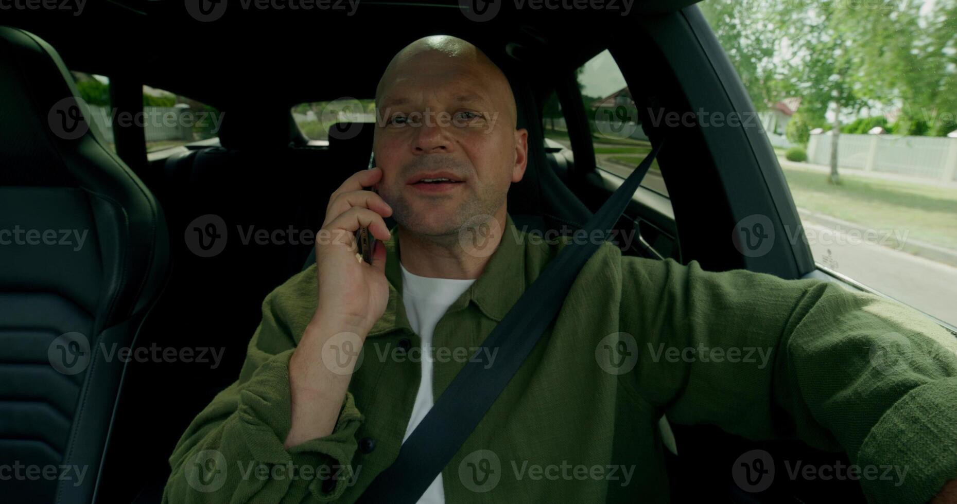 A man is talking on a mobile phone when driving a car. He's smiling. Front view in the car interior. Summer day photo