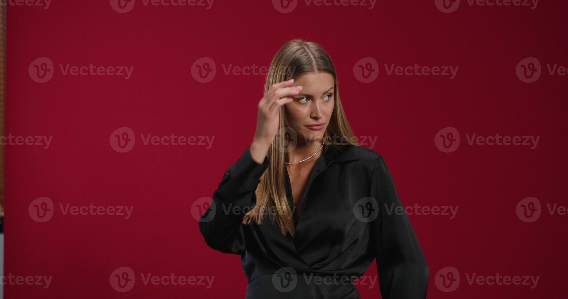 A woman in formal clothes smiles while looking at the camera posing in the studio. She touches her hair and her shirt photo