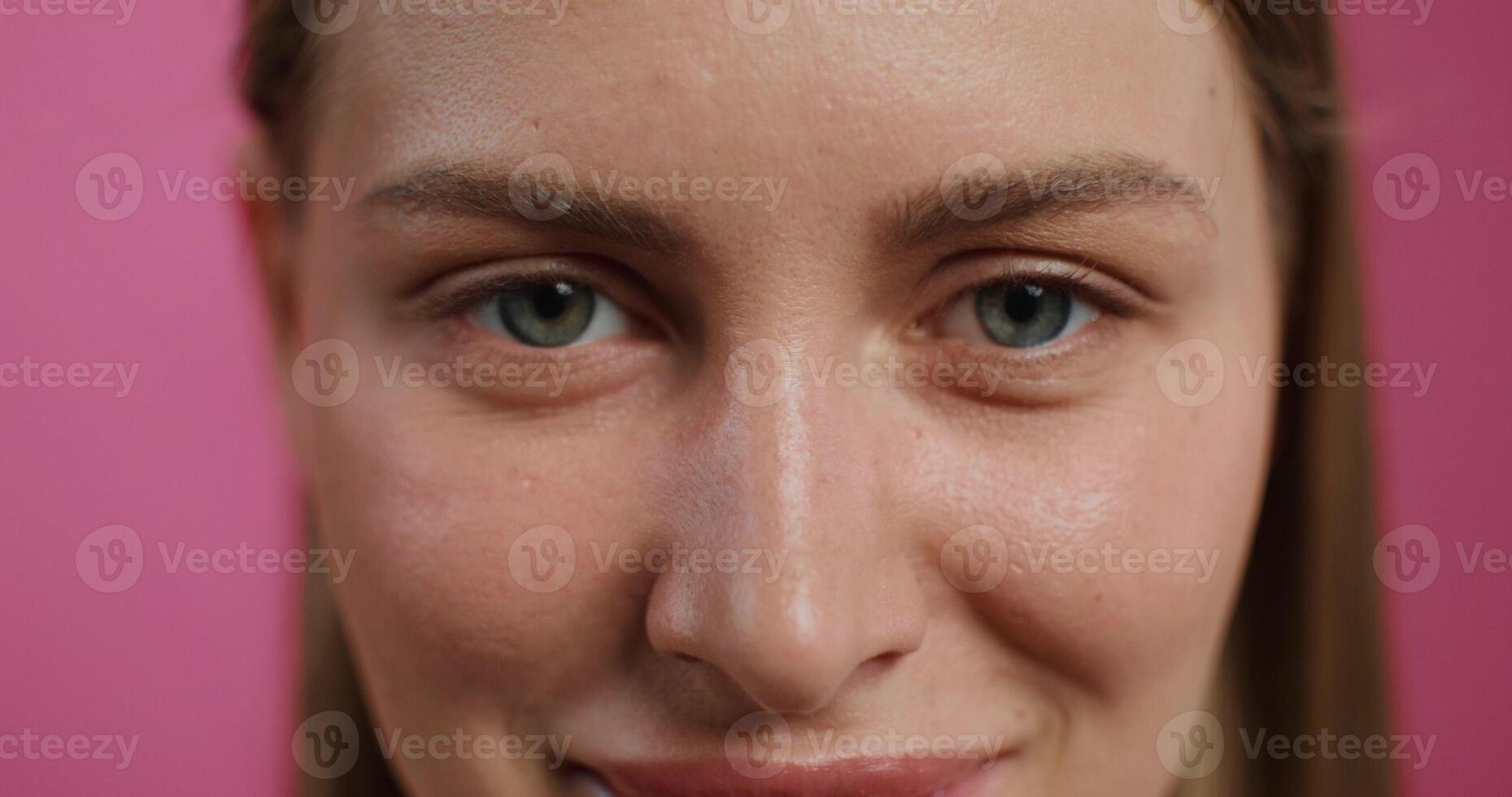 A woman smiles while looking at the camera standing on a pink studio background. Close-up of her face photo